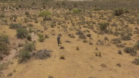 Holly Ratchford walks in the desert near where she now lives. There are mountains in the background.