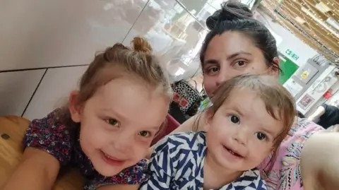 Harriet Anscombe London Mother Harriet Anscombe, her brunette hair piled atop her head in a bun, holds her mobile away from her to take a selfie with her two daughters, aged four and two