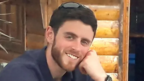 PA Media Andrew Harper is pictured - he is a man with short brown hair and a slight beard wearing a shirt and smiling at the camera.
