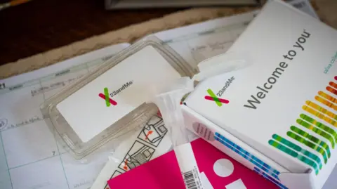 Getty Images A home DNA testing kit is spread out on a table, with a saliva collection tube and packaging prominently displayed. The branding 23andMe is clearly visible, as are the words 'Welcome to You' along with lots of coloured lines in the shape of a swab. 