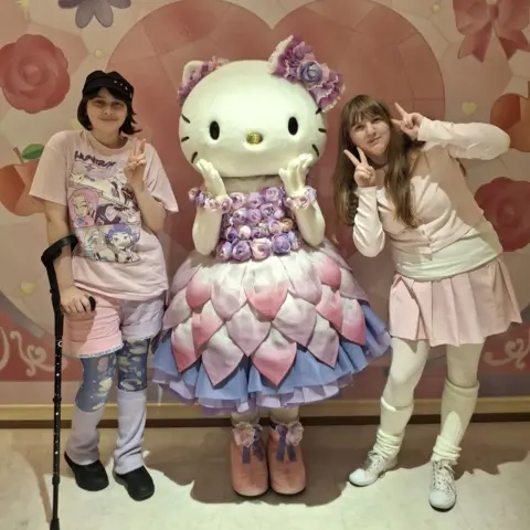 Millie Dring Two people in pastel colours stand next to a person in a Hello Kitty costume