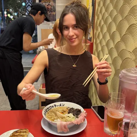 Faye Jawad Faye Jawad, in a brown top, sits in a restaurant and poses with a bowl of ramen