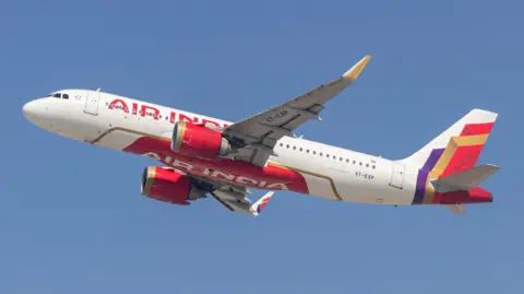 Getty Images An Air India plane - white with red lettering and a red, gold and purple pattern at the tail - flying against a blue sky 