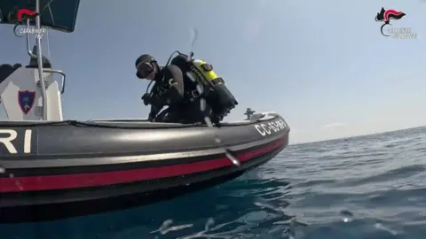 Carabinieri via AFP A diver in full scuba gear on the edge of a small boat in the sea