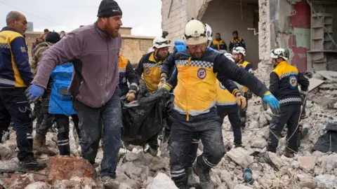 EPA Rescuers carry a body bag across rubble