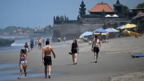 AFP via Getty Images Tourists walk on a beach in Bali