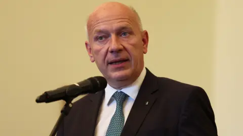 Reuters Berlin Mayor Kai Wegner speaks into a microphone on a pale yellow background wearing a dark suit and blue tie.