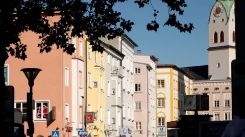 Getty Images Pastel-coloured buildings in Rosenheim, Bavaria, with a church tower with green roof seen at the end of the street, against a blue sky 