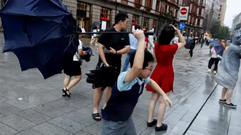 Reuters People holding umbrellas along a street in Shanghai. One boy is seen trying to hold on to an inverted umbrella as winds intensify