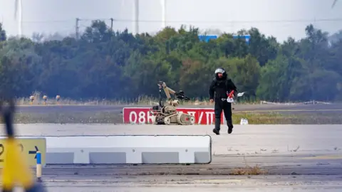 Jens Schlueter/Getty Images A police investigator works on the tarmac at Leipzig/Halle Airport on August 5, 2026, with a robot next to him