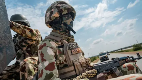 AFP via Getty Images Nigerian soldier in military uniform  sits in the back of a military escort vehicle along the Maiduguri-Damaturu highway on July 31, 2026
