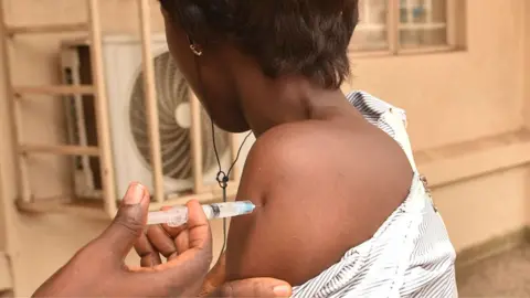 AFP via Getty Images A nurse injecting the arm of a health worker in West Africa with Ervebo - archive shot