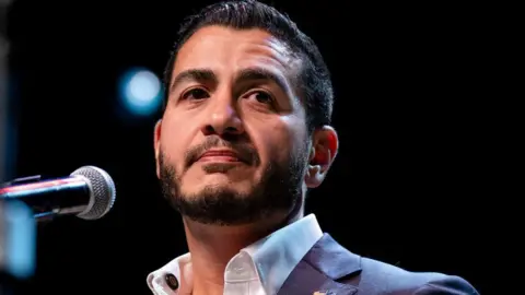 Getty Images Abdul El-Sayed on stage wearing an open necked white shirt and blue suit jacked, at an election night watch party at The Majestic Theatre in Detroit