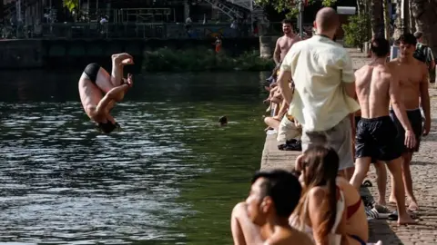 EPA/Shutterstock A man jumps into the water as people gather along the banks of the Canal Saint-Martin in Paris, France. Photo: 29 July 2026