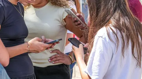 AFP via Getty Images Teenage girls use social media on their smartphones in France. Photo: July 2026
