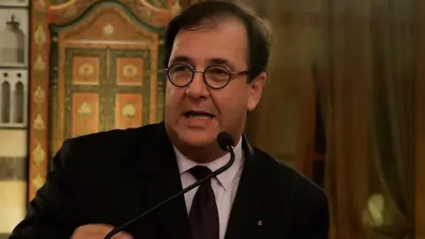 AFP via Getty Images Bruno Foucher in a black suit and tie and a white shirt speaks to a microphone