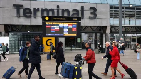 EPA Passengers push luggage outside Terminal 3 as a gate information screen can be seen in the background