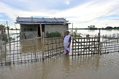 AFP via Getty Images A woman wades through floodwaters outside her inundated house at a village in Assam's Sivasagar 