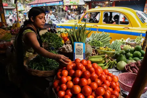 NurPhoto via Getty Images A  vegetable vendor waits for customers, displaying a barcode for Paytm, an Indian cellphone-based digital payment platform, at a market in Kolkata.