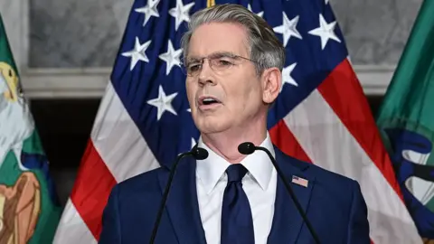 Getty Images US Treasury Secretary Scott Bessent speaks during a press conference at the Cash Room of the Treasury Department, as he announces a new set of sanctions against Iran. He is wearing a dark blue suit with a white shirt and dark blue tie. He has grey hair and wears glasses.