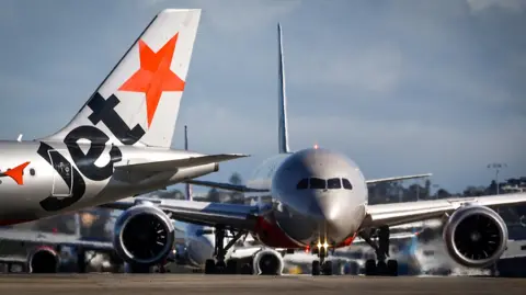 Getty Images The tail and nose of two Jetstar planes on the runway at Sydney International Airport