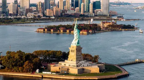 Getty Images aerial shot of Statue of Liberty and waters surrounding it with New York skyline in background