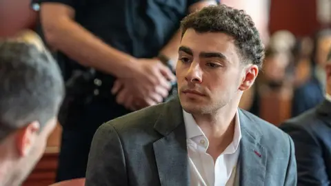 Getty Images Luigi Mangione wears a charcoal grey suit as he sits in court for a recent state hearing.