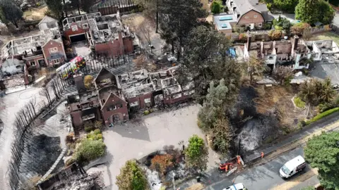 EPA An aerial image shows several houses destroyed by fire, with their roofs gone and wreckage visible within. There is a line of dead trees next to the houses and areas of scorched earth. A fire engine is parked by one of the houses.