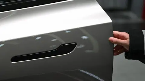 AFP via Getty Images A customer inspects the minimalistic hidden door handles on an electric car in a showroom. 