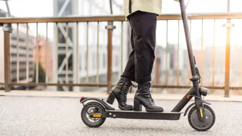 Maskot via Getty Images An e-scooter being ridden by someone wearing high-heel boots, in close-up