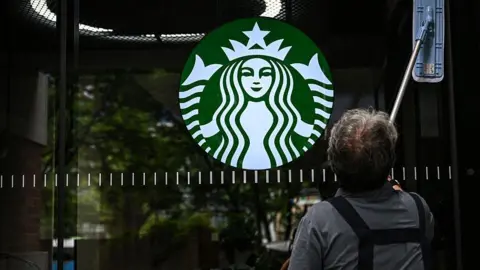 AFP via Getty Images A cleaning lady wipes the window of a Starbucks coffee shop