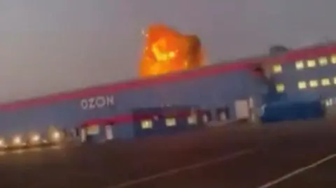 Reuters A screengrab from a video on social media showing flames rise from an Ozon facility following a Ukrainian drone strike in Makhachkala, Dagestan, Russia.