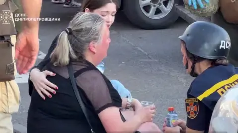 DSNS / Dnipropetrovsk region A psychologist talks to a distressed woman after a Russian drone attack in Kryvyi Rih, central Ukraine. Screenshot from a video by Ukraine's state emergencies service DSNS