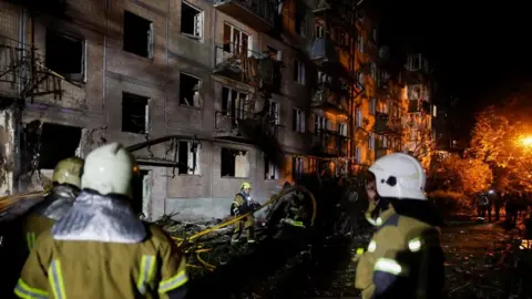 Reuters Firefighters work at the site of an apartment building hit by a Russian missile strike in Kyiv