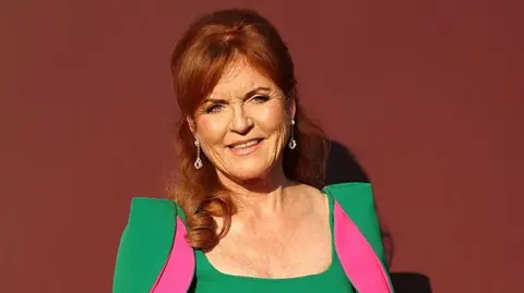 Getty Images Sarah Ferguson, with her dark red hair half tied up, in a green dress and fuchsia dress and diamond earrings