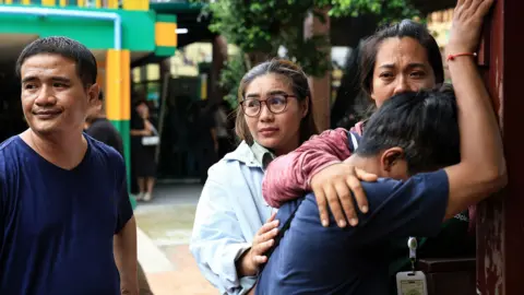 Getty Images  A person close to one of the victims reacts by leaning their head against a wall, people nearby comfort him. 