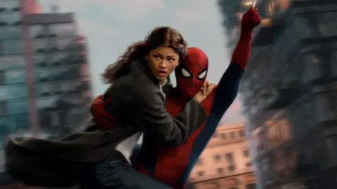 Sony Pictures/Marvel Spider-Man swings through the city on web whilst holding MJ, played by Zendaya.