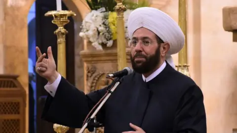AFP via Getty Images File photo showing Syria's then grand mufti, Ahmed Hassoun, speaking inside the Cathedral of Mar Elias in the northern Syrian city of Aleppo on 20 July 2020
