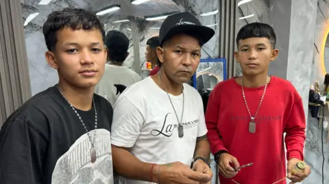 BBC Mundo Two teenage boys stand either side of their father.