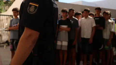 Reuters A police officer stands guard as migrant children queue outside a police station in Ceuta to be registered following mass crossings by migrants on foot and by sea from Morocco.