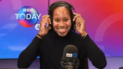 BBC Holding headphones on his head, BBC Radio 4 Today Christmas guest editor Prof Jason Arday smiles at the camera in the studio. 