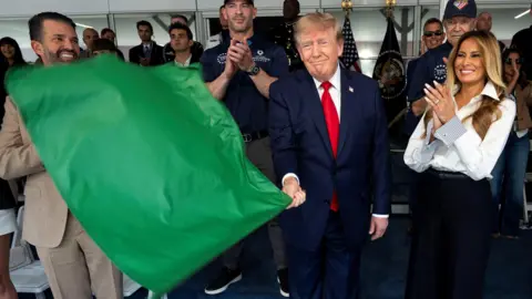 Reuters Donald Trump waves a green flag as he stands next to his wife Melania who is smiling and clapping
