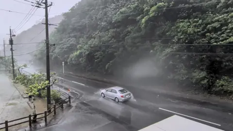 X/Reuters A car makes its way through strong winds and rain as Typhoon Dolphin approaches, in Nazeasahicho, Amami, Kagoshima, Japan, August 7, 2026, in this screengrab obtained from a social media video. 