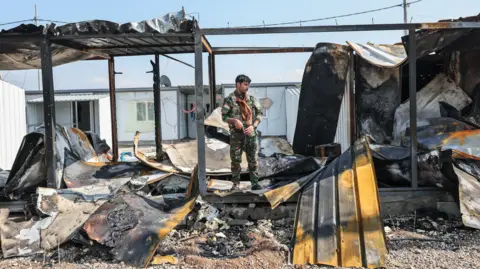 Getty Images A member of Kurdistan Freedom Party stands next to damaged containers at their military base in Irbil, Iraq, after Iranian drone attack in March
