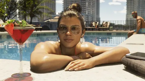 Rockstar Games Screenshot from GTA 6 shows Lucia resting her elbows on the corner of a swimming pool next to what appears to be a rooftop hotel bar. A cocktail glass is on her right and a mobile phone on top of a folded towel is on her left.