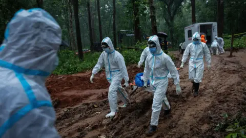 Reuters People in white PPE carry a stretcher with a dead body on it in a forest