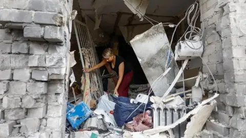 Reuters A woman in Ukraine's town of Boryspil, outside Kyiv, collects belongings from her flat destroyed by overnight Russian strikes. Photo: 1 September 2026