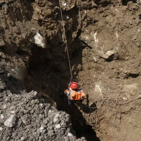 Reuters A rescue worker lowering themselves into a hole ata hydropower site