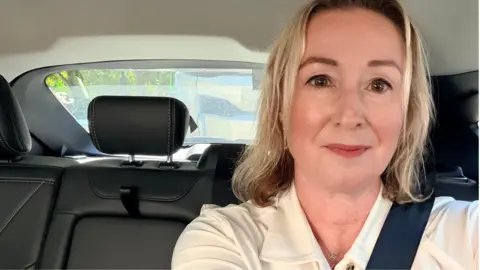 A selfie of Zoe in the back of a driverless robotaxi, wearing a cream blouse and wearing a seatbelt.