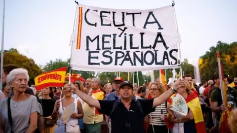 Reuters Protesters hold flags and a sign during a demonstration in support of residents of Spain's North African enclave of Ceuta following recent mass crossings of migrants from Morocco, in Madrid, Spain, September 2, 2026.